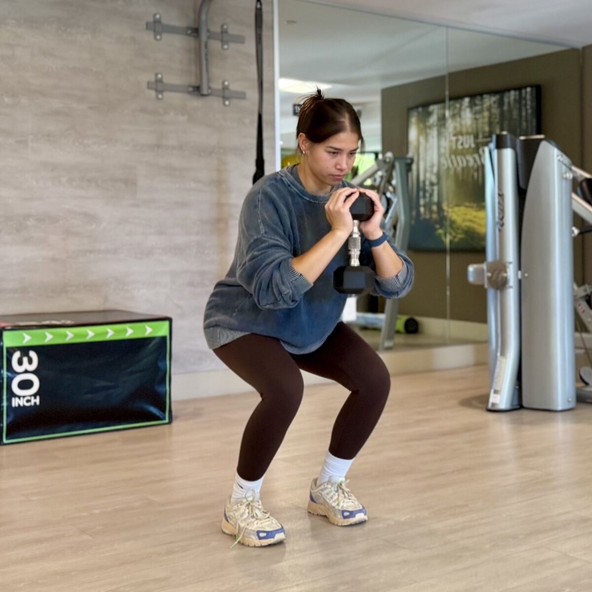 Woman performing a goblet squat with a dumbbell during a personal training session, maintaining focus and form in a clean, modern gym setting.